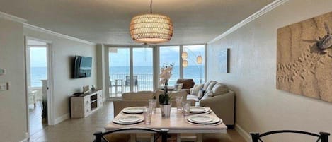 A dining area with a table set for four, a sofa, and a view of the ocean through large windows.