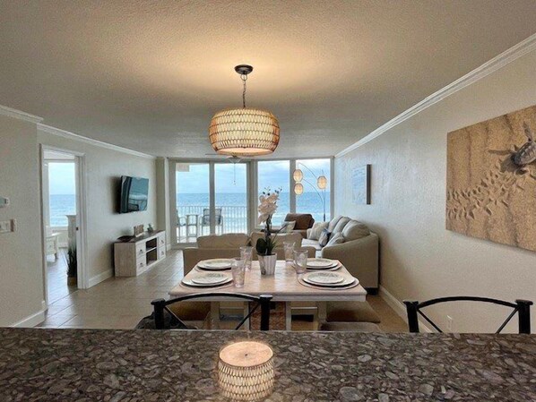 Un coin repas avec une table dressée pour quatre personnes, un canapé et une vue sur l’océan grâce à de grandes fenêtres.