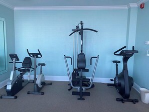 Un gimnasio en casa con tres máquinas de ejercicio, un cubo de basura blanco y una pared azul claro.