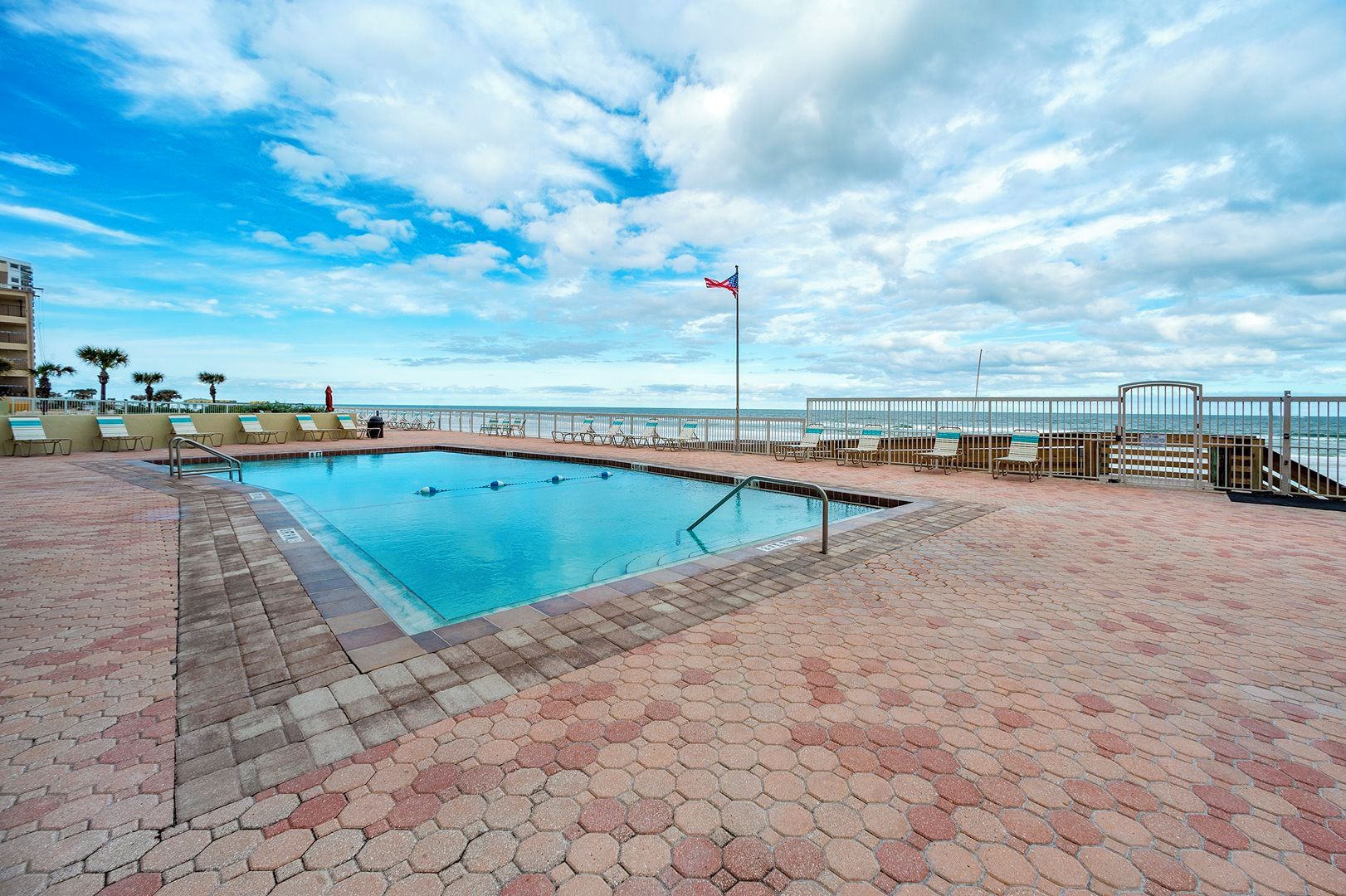 A swimming pool with a view of the ocean, surrounded by lounge chairs and a fence.