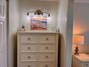 A corner with a white dresser, a framed artwork above it, and a small lamp on a side table.