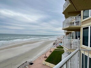 A beachfront hotel with balconies overlooking the ocean, a pool area, and a well-maintained lawn.