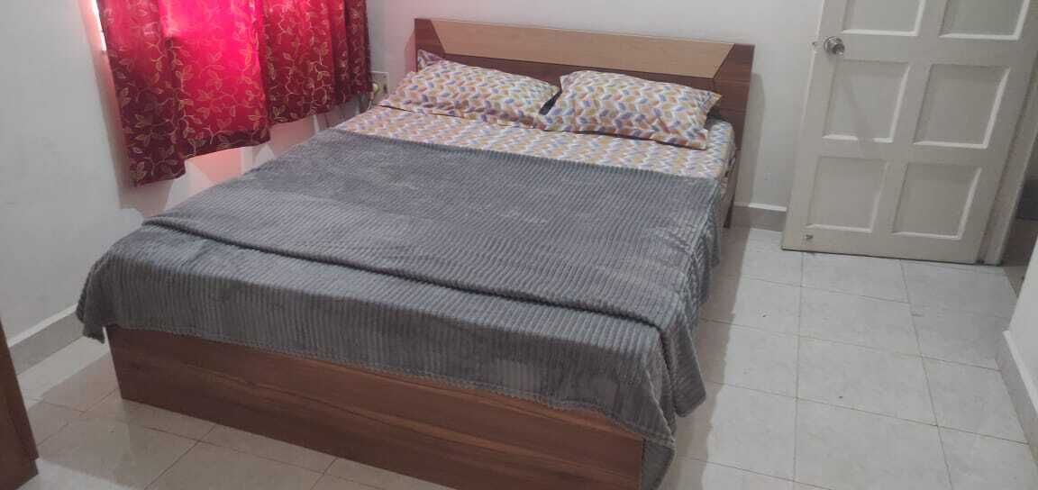 A bed with a grey bedspread and patterned pillows, a wooden headboard, and a red curtain.