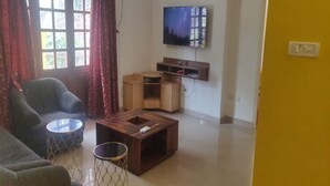 A living room with a sofa, a coffee table, a TV mounted on the wall, and a wooden cabinet. - Signum Court (Calangute)