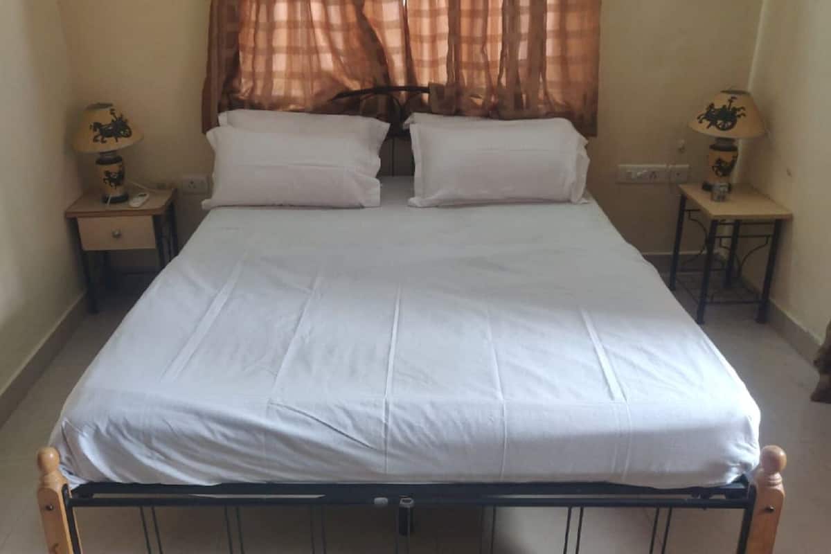 A standard single bed with a metal frame, two bedside tables, and a window with sheer curtains.