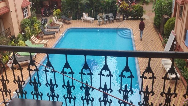 A swimming pool with lounge chairs and a person walking nearby. - Signum Court (Calangute)
