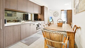 A modern kitchen with wooden cabinets, a dining table with chairs, and a clock on the wall.