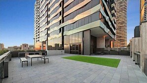 A modern building with a rooftop patio featuring outdoor seating and a green lawn.