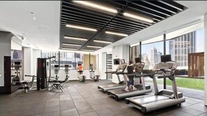 A modern gym with treadmills, weight machines, and a large window offering a city view.