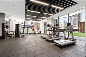 Ein modernes Fitnessstudio mit Laufbändern, Kraftgeräten und einem großen Fenster mit Blick auf die Stadt.