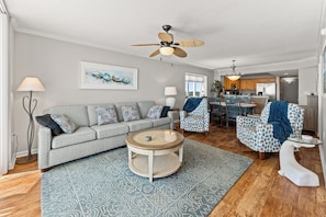 A modern living room with a grey sofa, patterned armchairs, a round coffee table, and a ceiling fan.