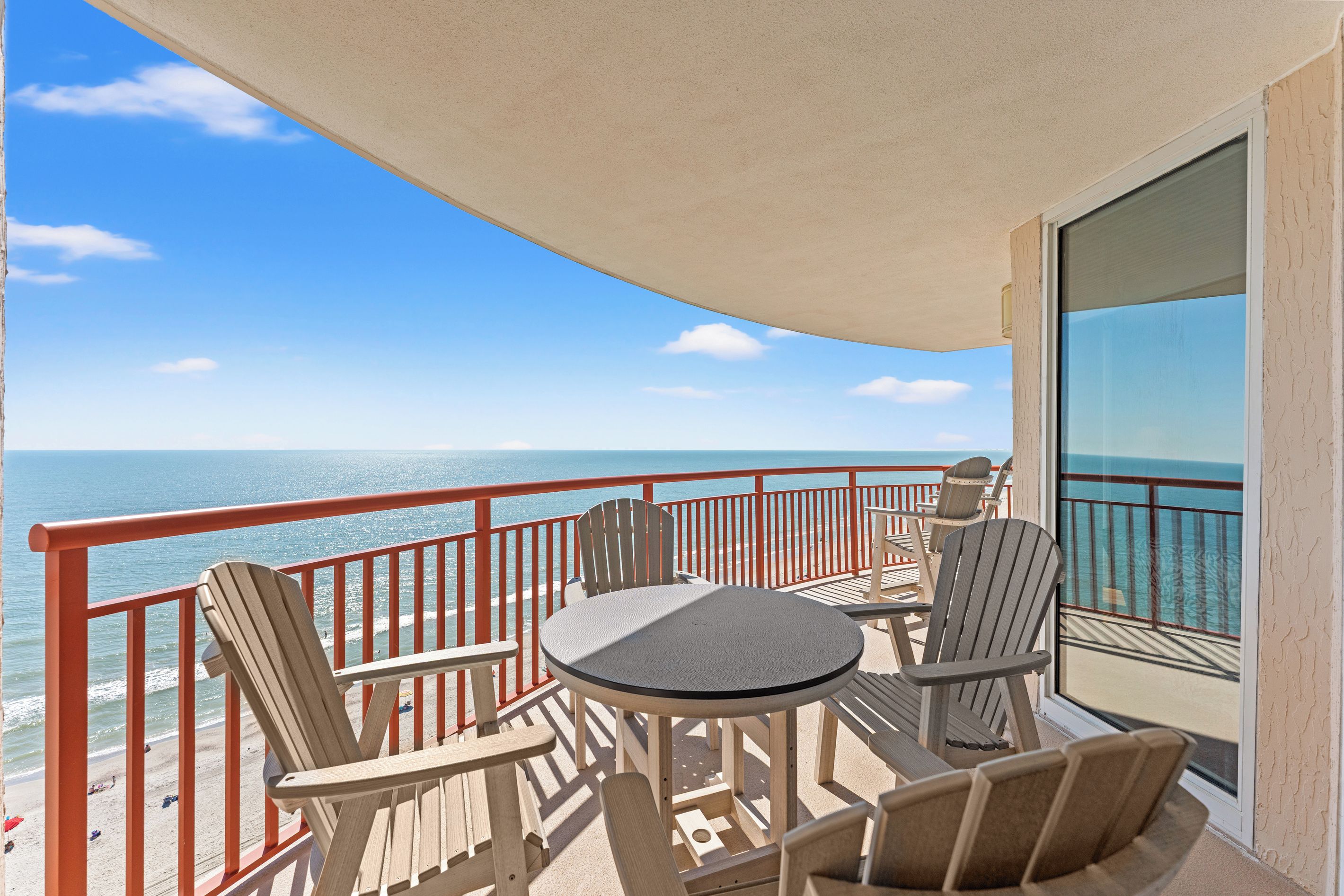 A balcony with a table and chairs, overlooking a beach and the ocean.