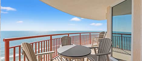 A balcony with a table and chairs, overlooking a beach and the ocean.