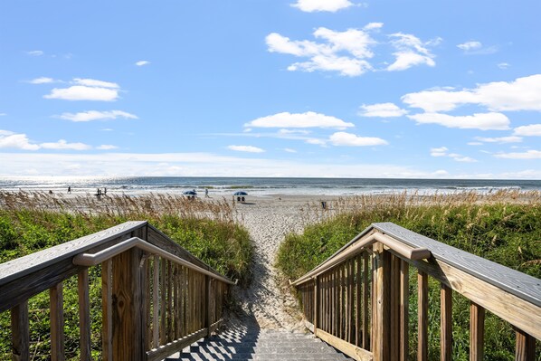 A wooden pathway leading to a beach with a clear sky and a few people in the distance.