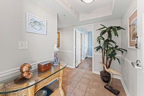 A hallway with a wooden console table, a framed crab artwork, a potted plant, and a door leading to another room.