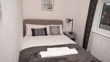 A neatly made bed with a fluffy gray blanket and white towels, a framed picture on the wall, and a bedside lamp.