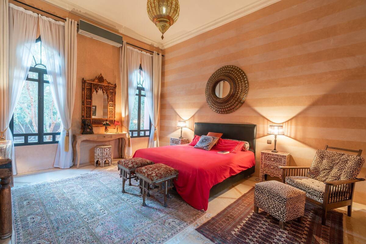 A spacious bedroom with a large bed, two bedside tables with lamps, a wooden chair, and a patterned rug.