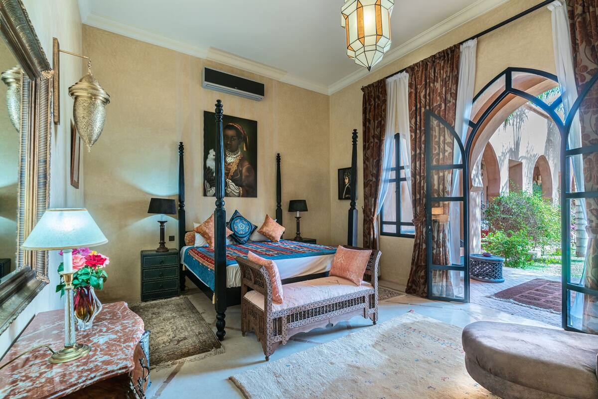 A bedroom with a bed, bedside tables, a lamp, a mirror, and an arched window.