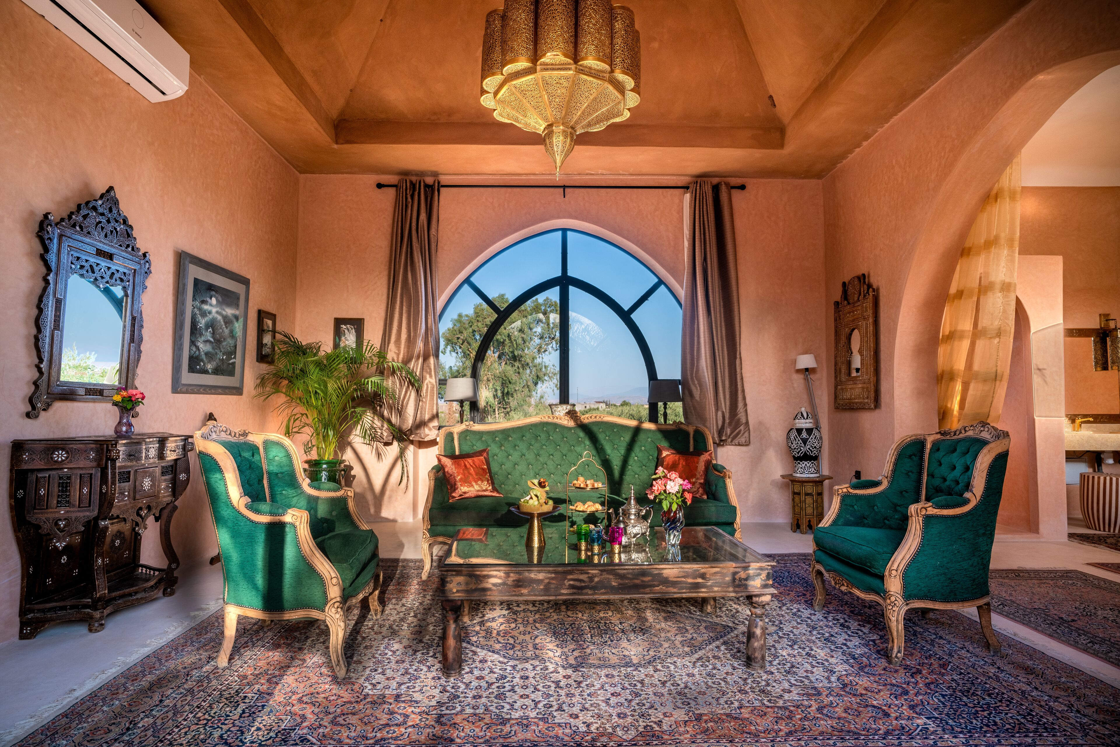 A room with a green sofa, two green armchairs, a coffee table, and a large arched window.