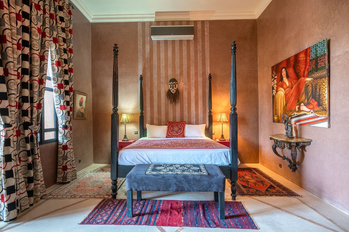 A four-poster bed with a red and white bedspread, a bench at the foot of the bed, and a large painting on the wall.