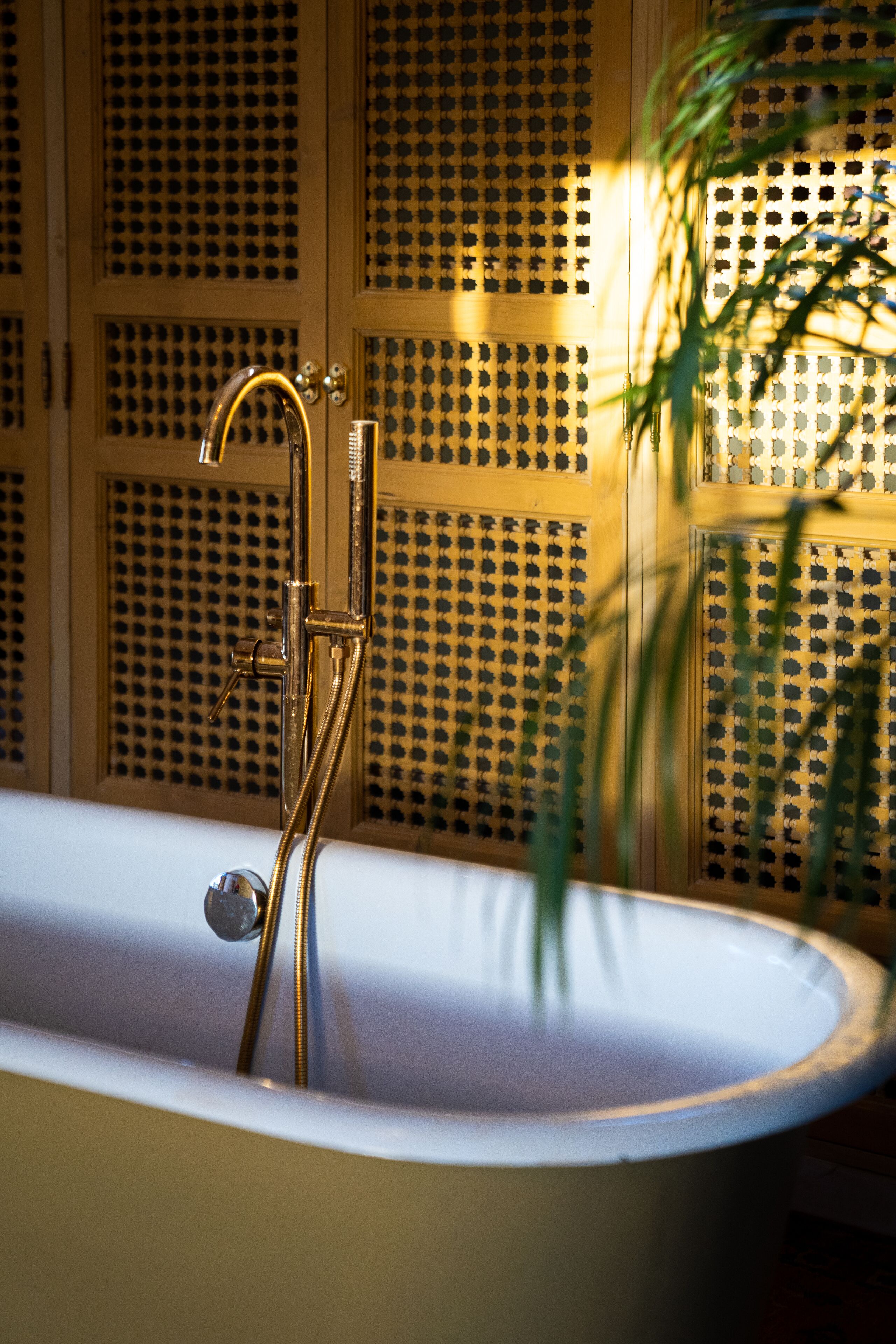 Una bañera con grifo y manguera dorados, frente a una pared con diseño decorativo.