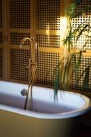 Una bañera con grifo y manguera dorados, frente a una pared con diseño decorativo.
