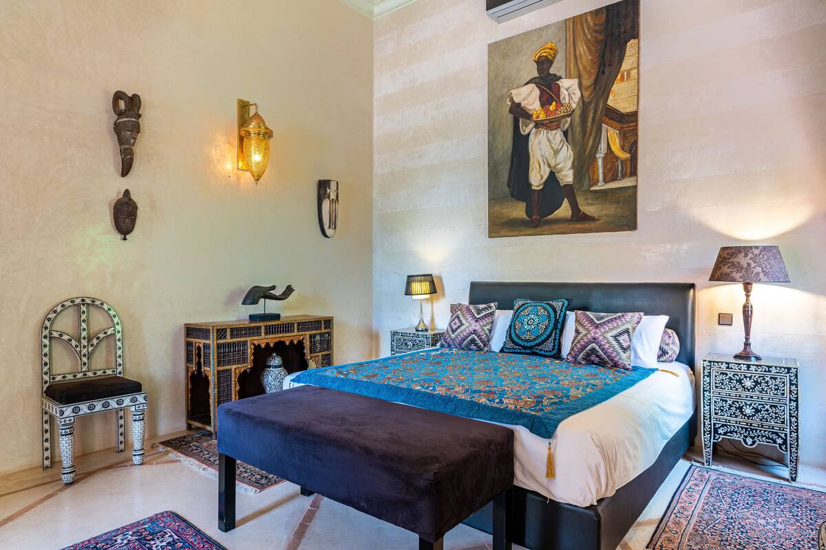 A bedroom with a large bed, two nightstands, a chair, and a wall with decorative items.