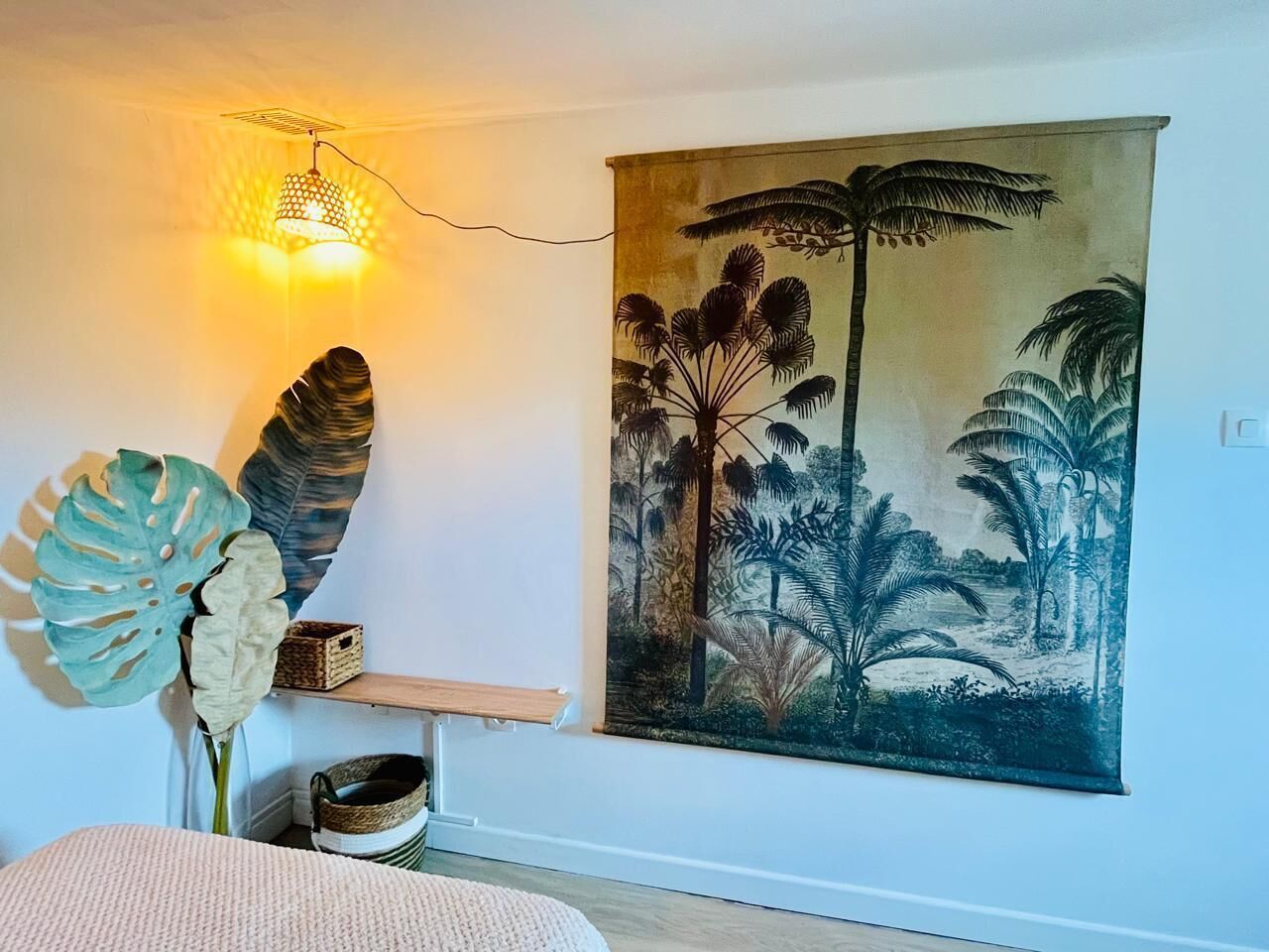 Una habitación con un cuadro de gran tamaño con temática tropical, una escultura de hoja grande y un aplique de pared.