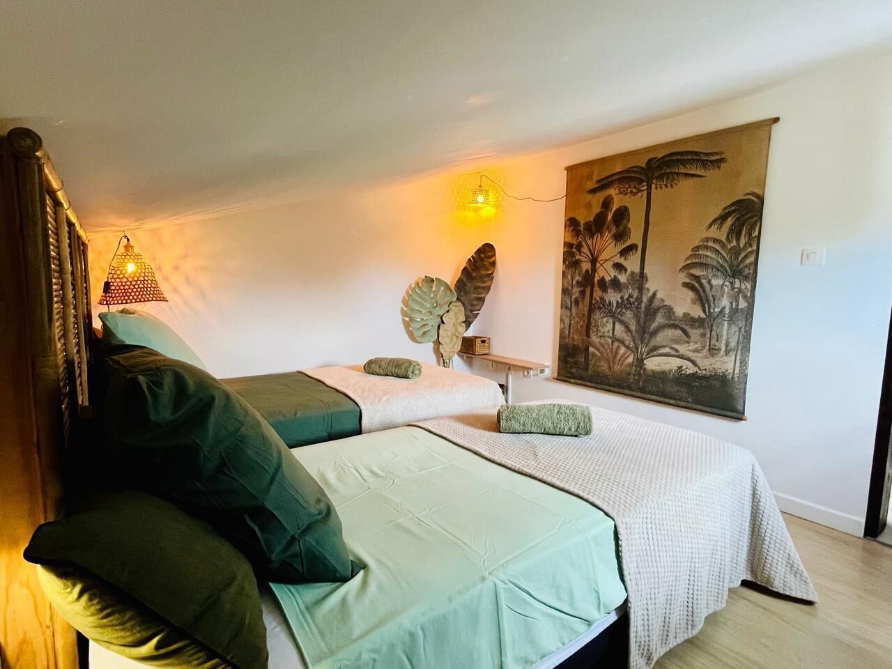 Una habitación con dos camas, un cuadro grande y una lámpara fijada a la pared.