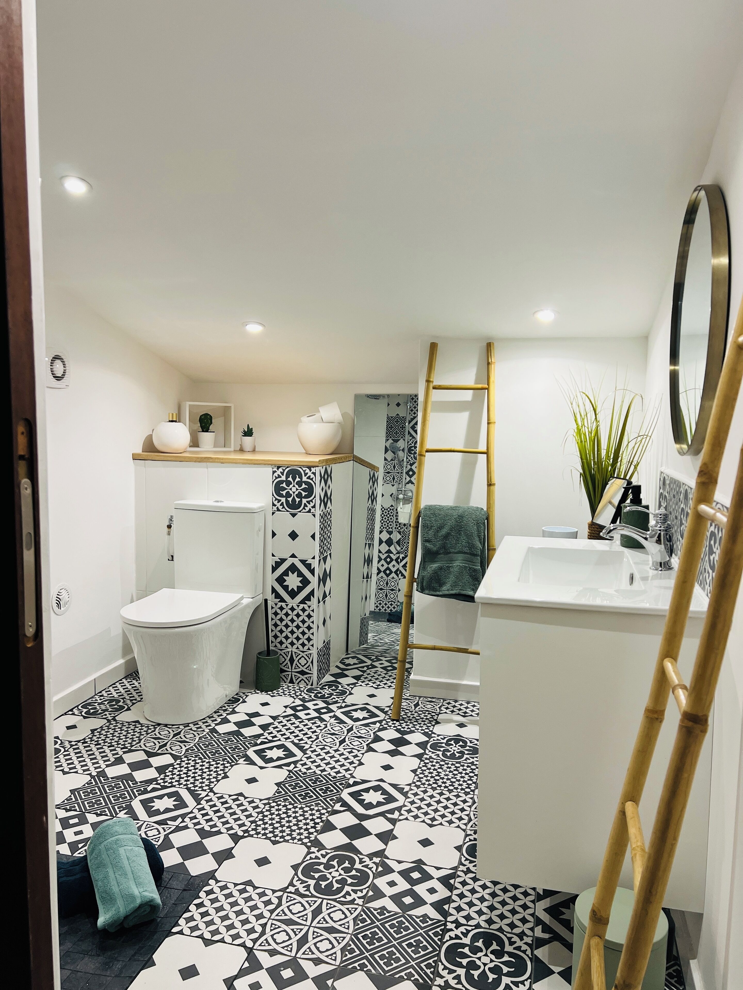 A bathroom with a toilet, sink, and shower area. There is a patterned floor and a mirror above the sink.