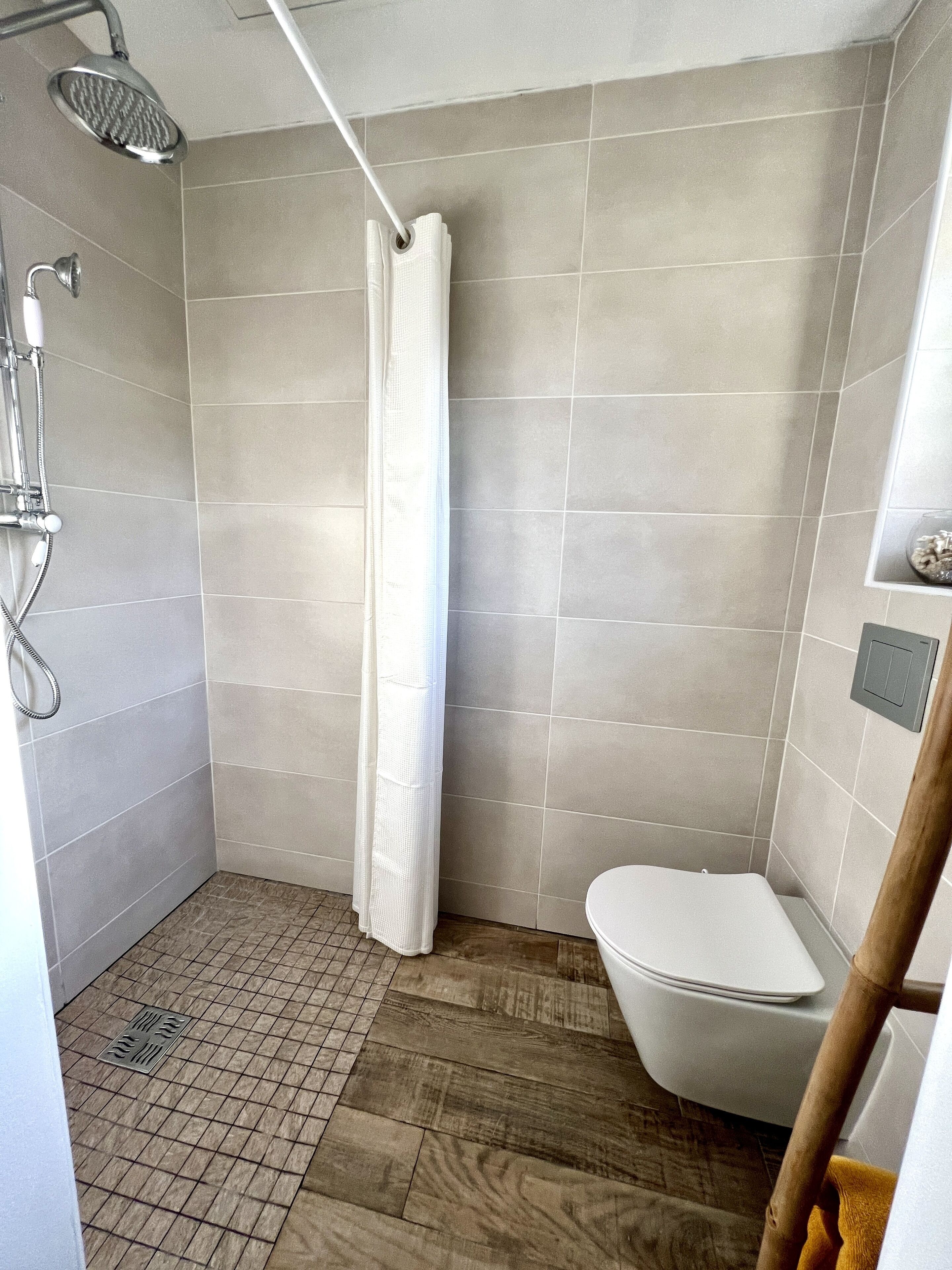 Un baño pequeño y moderno con ducha, inodoro y suelo de madera.