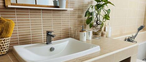 Un bagno con lavandino bianco, uno specchio, una pianta e articoli da toilette sul ripiano.