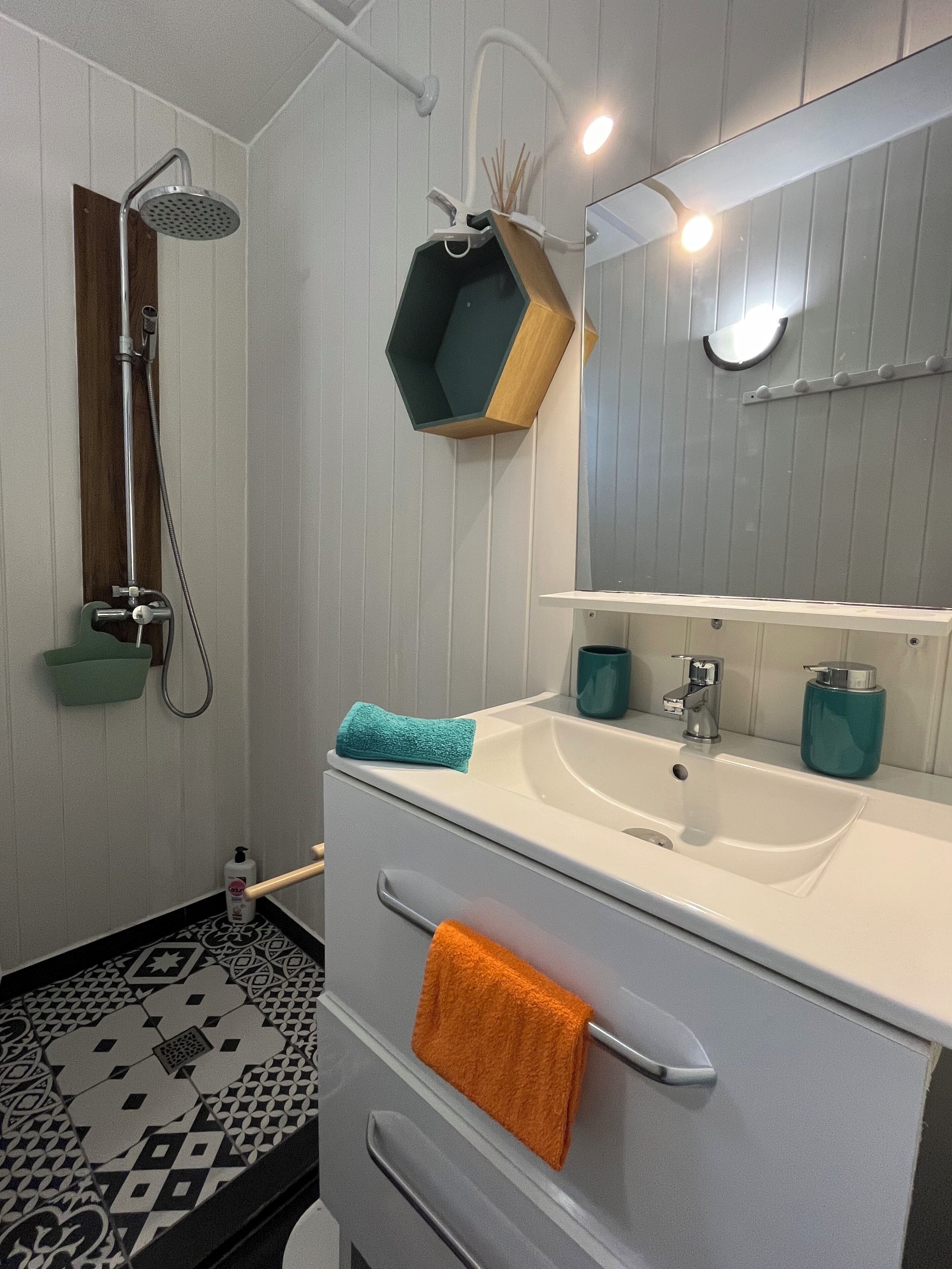 Et moderne badeværelse med bruser, håndvask med spejl og et håndklædetørrestativ.