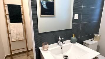 A modern bathroom with a large white sink, a mirror, and a framed artwork on the wall.