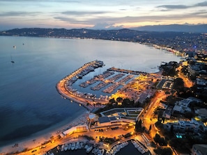 An aerial view of a marina with boats docked, a parking area, and buildings along the waterfront.
