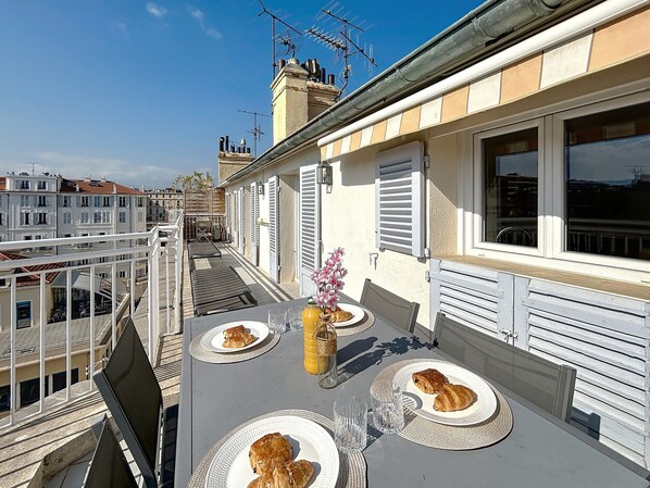 A balcony with a table set for breakfast, including croissants and a vase with flowers.