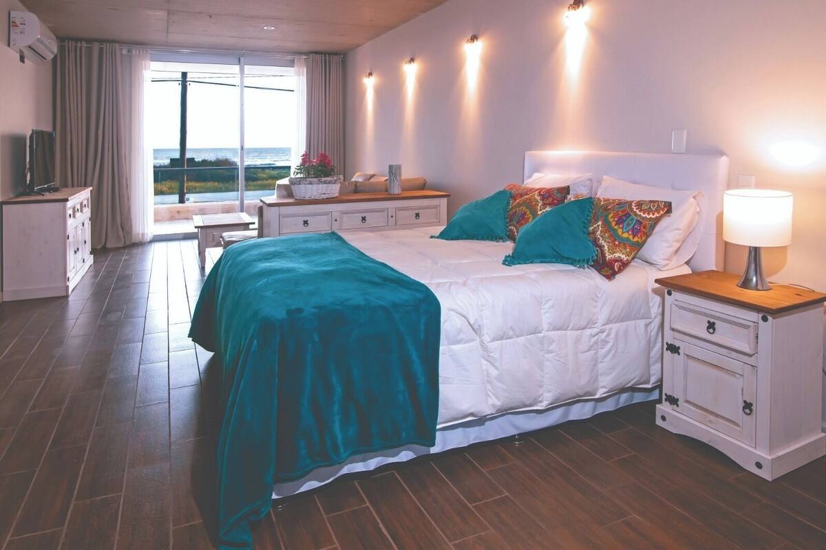 Een slaapkamer met een groot bed, een nachtkastje met een lamp, een dressoir en uitzicht op de omgeving.
