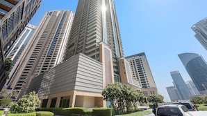 A modern high-rise building with a prominent corner design, surrounded by other tall buildings and greenery. - Silkhaus - 8 BLVD Walk (Dubai)