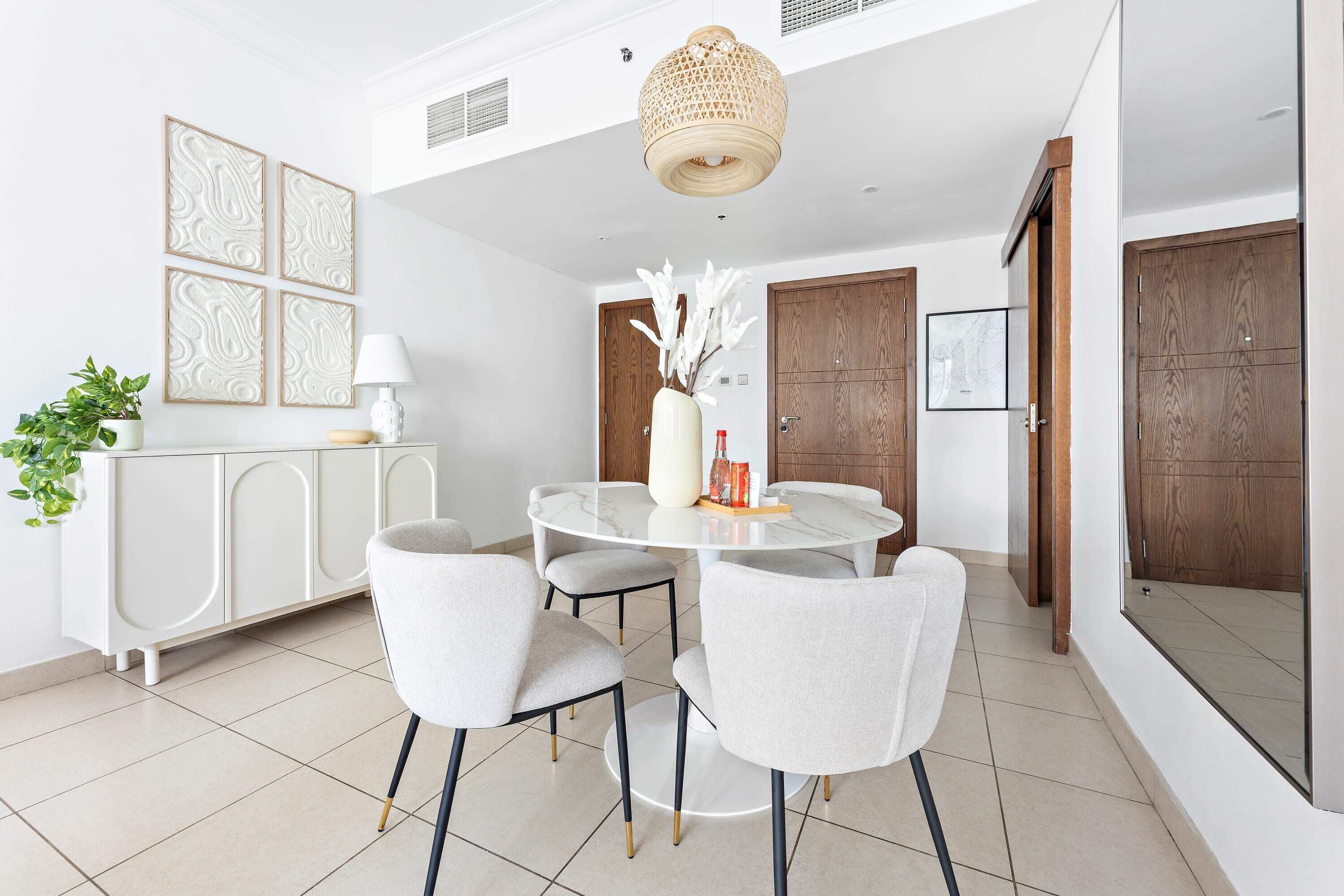 A modern dining area with a round table, four chairs, a white cabinet, and a hanging light fixture.