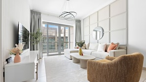 A modern living room with a sofa, coffee table, and a unique textured armchair. A flat-screen TV is mounted on the wall, and there is a large window with curtains. - Silkhaus - 8 BLVD Walk (Dubai)