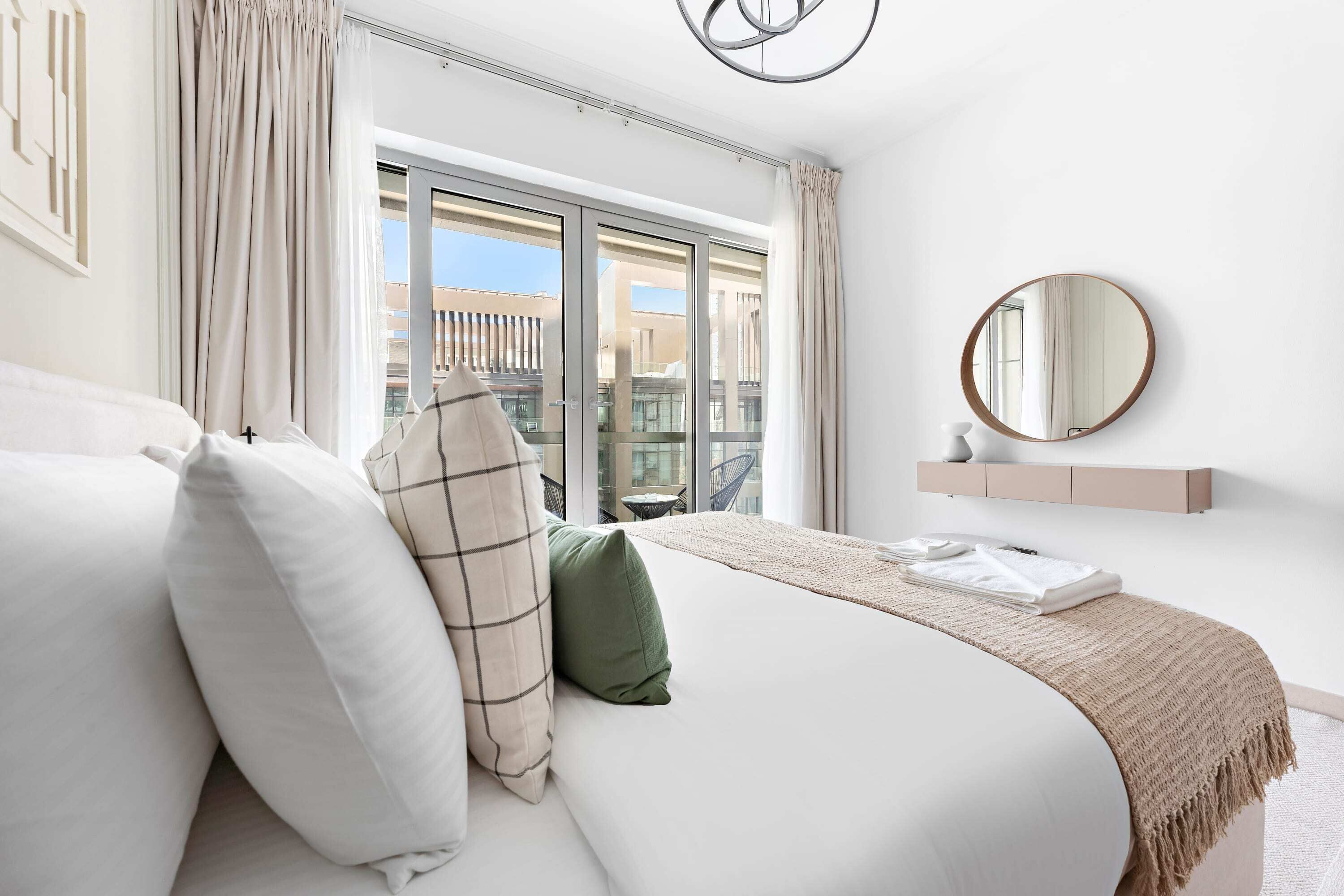 Un dormitorio moderno con una cama grande, vistas de la ciudad a través de una puerta corredera, un espejo redondo y una decoración de estilo minimalista.