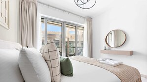 A modern bedroom with a large bed, a view of the city through a sliding door, a round mirror, and a minimalist decor style. - Silkhaus - 8 BLVD Walk (Dubai)
