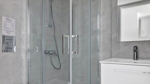 A modern bathroom with a glass-enclosed shower, a white sink, and a mirror above the sink. - Phaedrus Living: Alkminis Seaview Suites Pantai (Paphos)