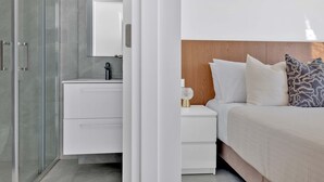 A modern bedroom with a wooden headboard, white bedding, and a bedside table with a lamp. - Phaedrus Living: Alkminis Seaview Suites Pantai (Paphos)