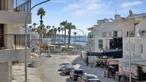 A street view with parked cars, buildings, and a view of the sea. - Phaedrus Living: Alkminis Seaview Suites Pantai (Paphos)