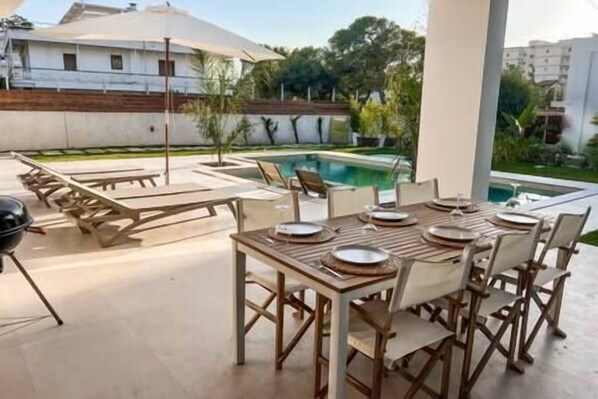 An outdoor dining area with a pool in the background.