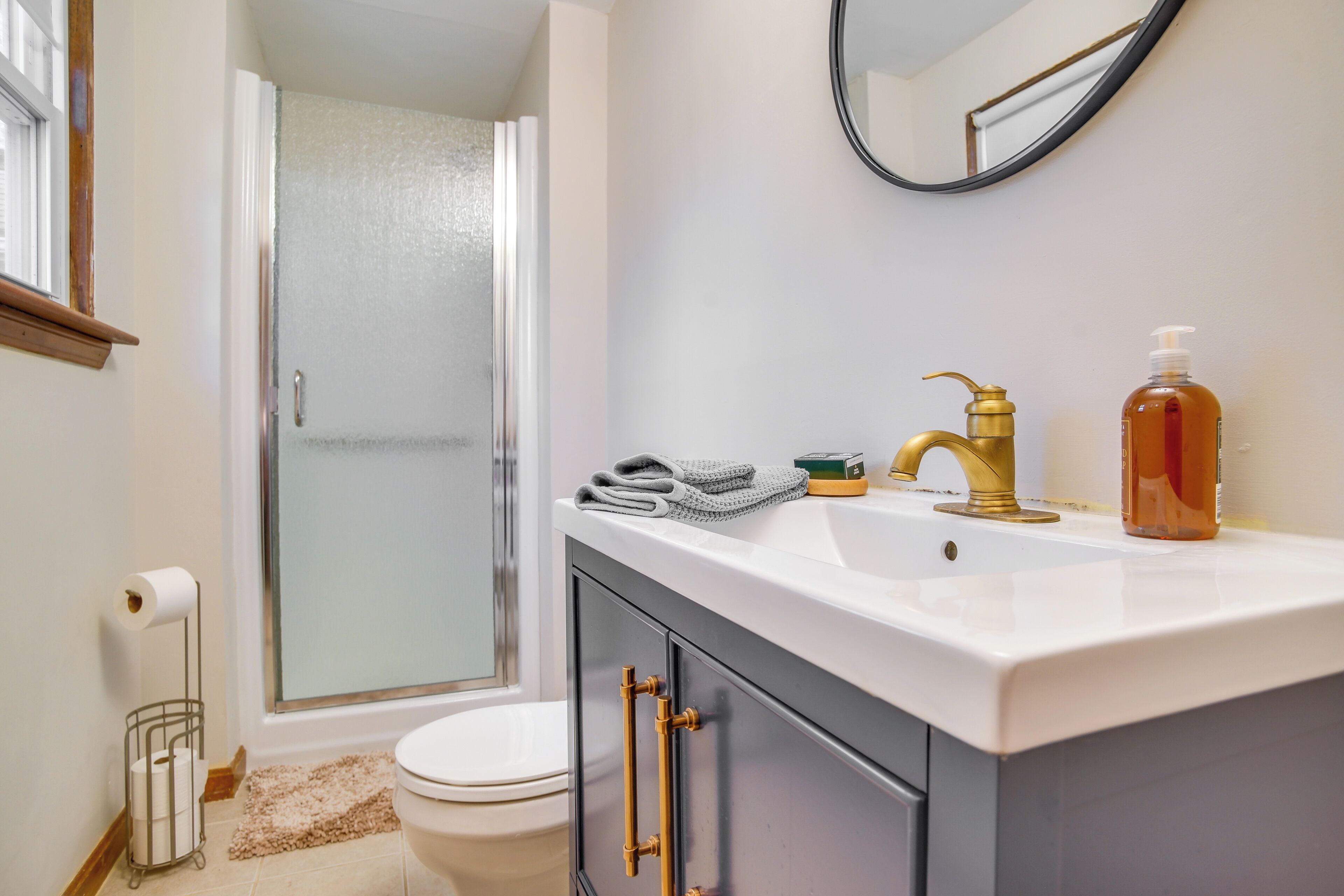 Une salle de bain avec un lavabo blanc, un robinet doré et un miroir au-dessus. Il y a une serviette sur le lavabo et un flacon de savon sur le comptoir.