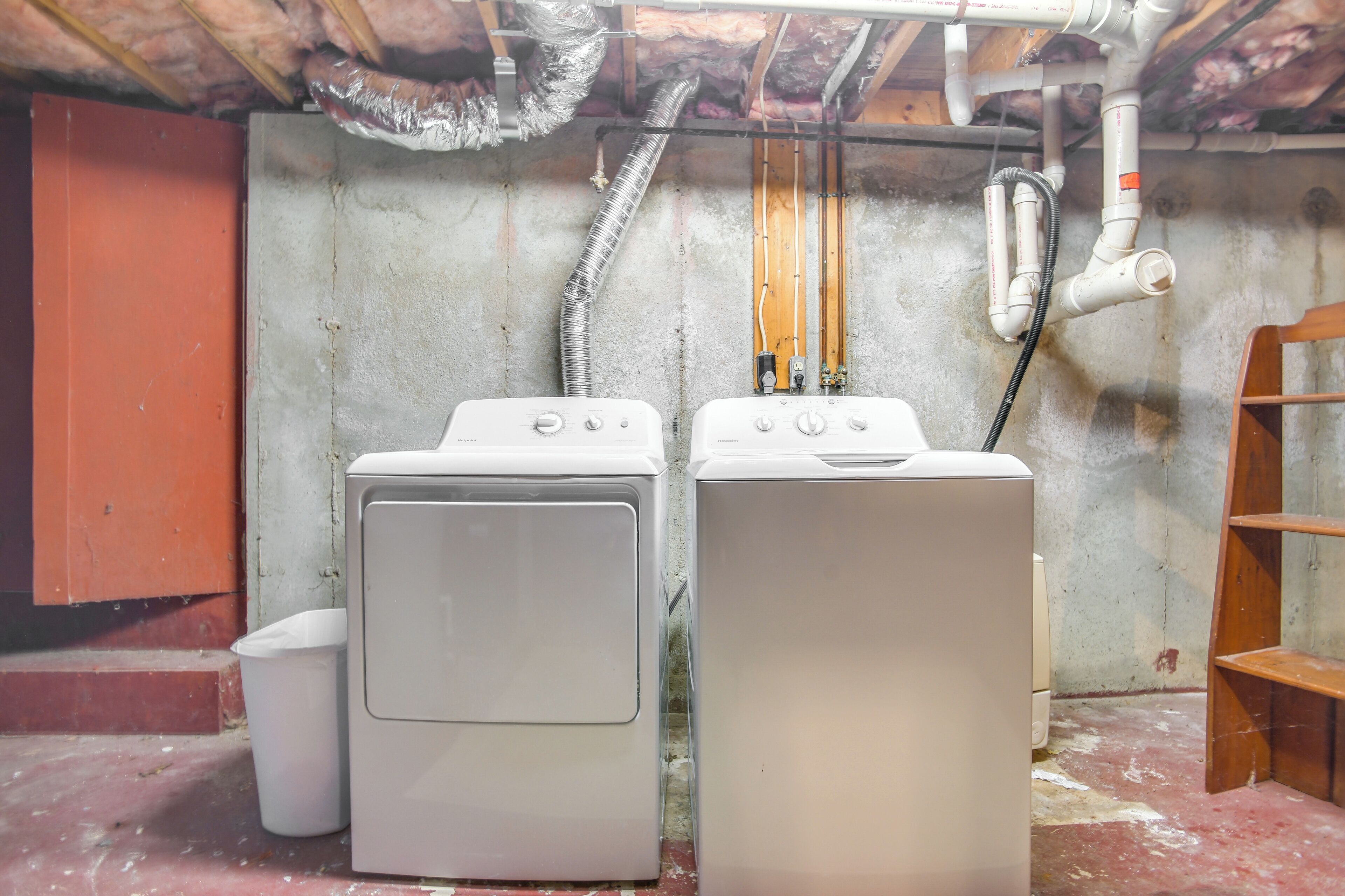 A laundry room with two washing machines, a metal vent, and a wooden shelf.