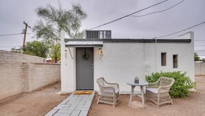A small, single-story building with a white exterior, a gray door, and a small porch area with two wicker chairs and a table. - Tucson Studio ~ 2 Mi to University of Arizona! (Tucson)