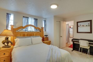 Ein Schlafzimmer mit einem hölzernen Bett, einem Nachttisch mit Lampe, einem Schreibtisch mit Stuhl und einem Klavier.